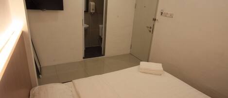 A hotel room with a bed, a TV mounted on the wall, a door, and a small bathroom visible through an open door.