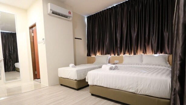 Habitación de hotel con dos camas, un ventanal con cortinas oscuras, un aire acondicionado montado en la pared y un espejo que refleja parte de la habitación.