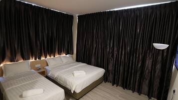 Una habitación de hotel con dos camas, cortinas oscuras, una mesita de noche con lámpara y suelo de madera.