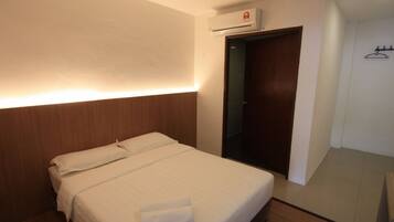 Habitación de hotel con una cama bien hecha, un cabecero de madera, aire acondicionado montado en la pared y una puerta que da a un armario.