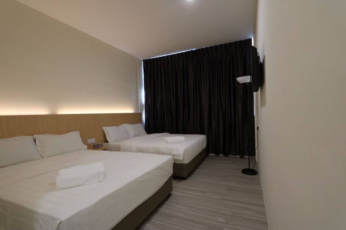 A hotel room with two beds, a dark curtain, a wall-mounted light, and a wooden headboard.