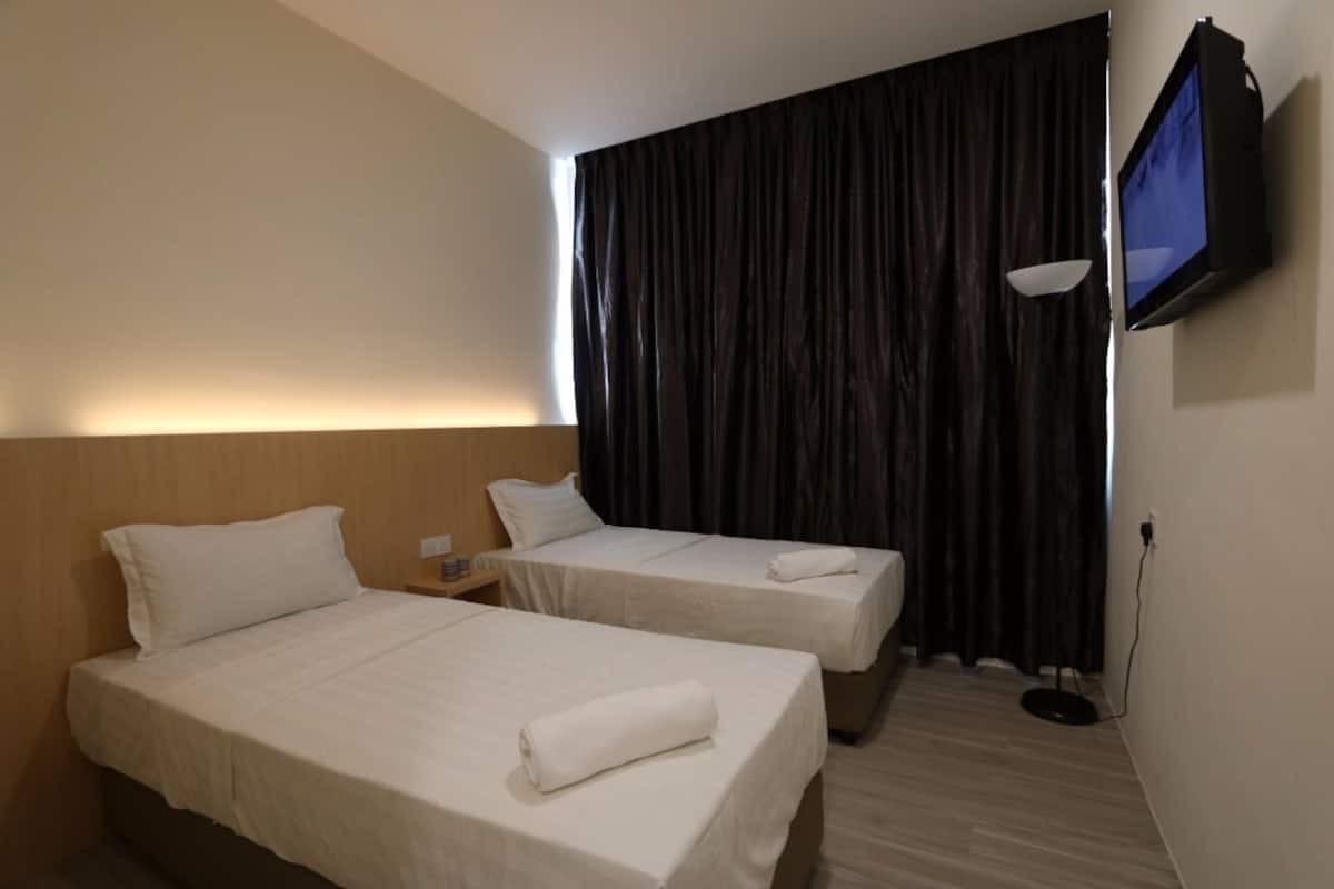 A hotel room with two single beds, a flat-screen TV mounted on the wall, and a large window with dark curtains.
