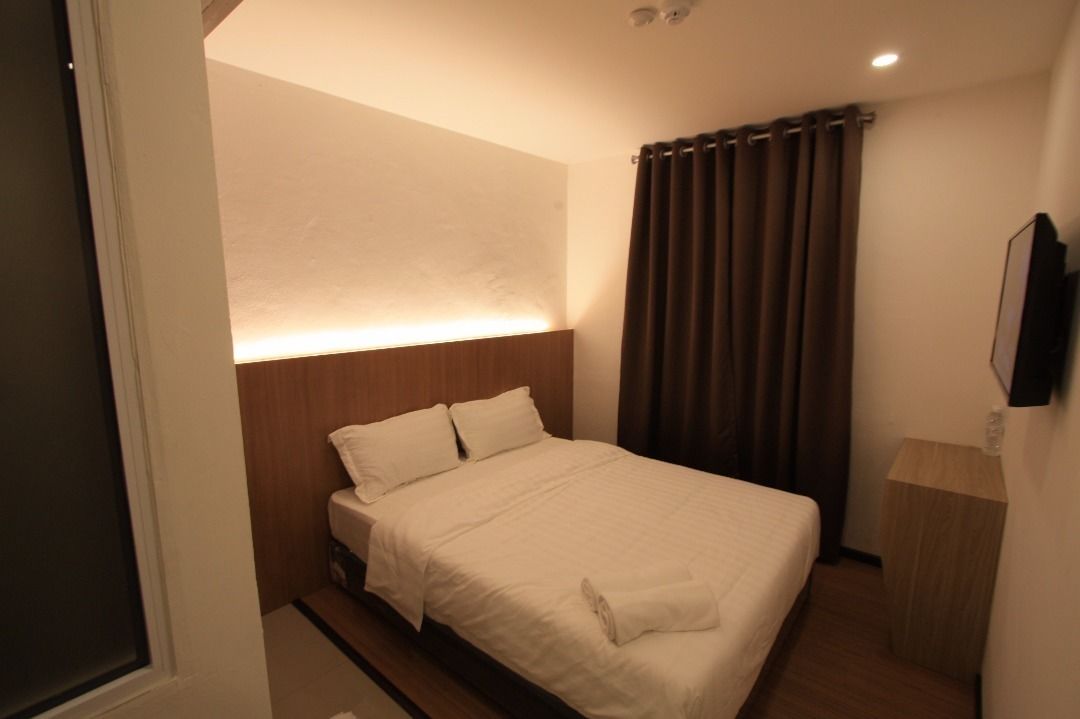 A hotel room with a bed, a nightstand, a wall-mounted TV, and a curtain.
