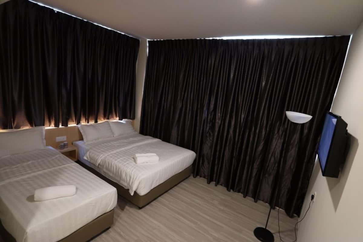 A hotel room with two beds, a flat-screen TV, a bedside lamp, and a window with curtains.