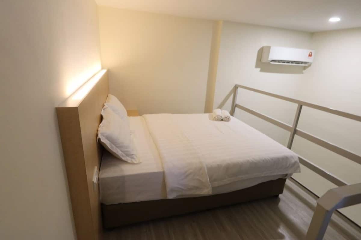 A single bed with white bedding, a bedside table with a lamp, and an air conditioning unit on the wall.
