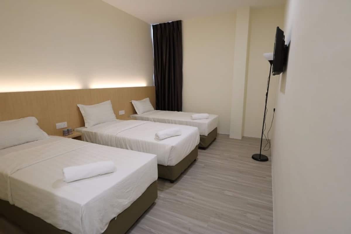 A hotel room with three single beds, a flat-screen TV mounted on the wall, and a floor lamp.