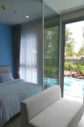 A bedroom with a bed, a sofa, and a sliding glass door leading to a pool area.