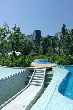 A swimming pool with a curved design, surrounded by greenery and a cityscape in the background.