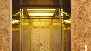 Un ascensor con pantalla digital, interior metálico y puertas de vidrio con diseño.