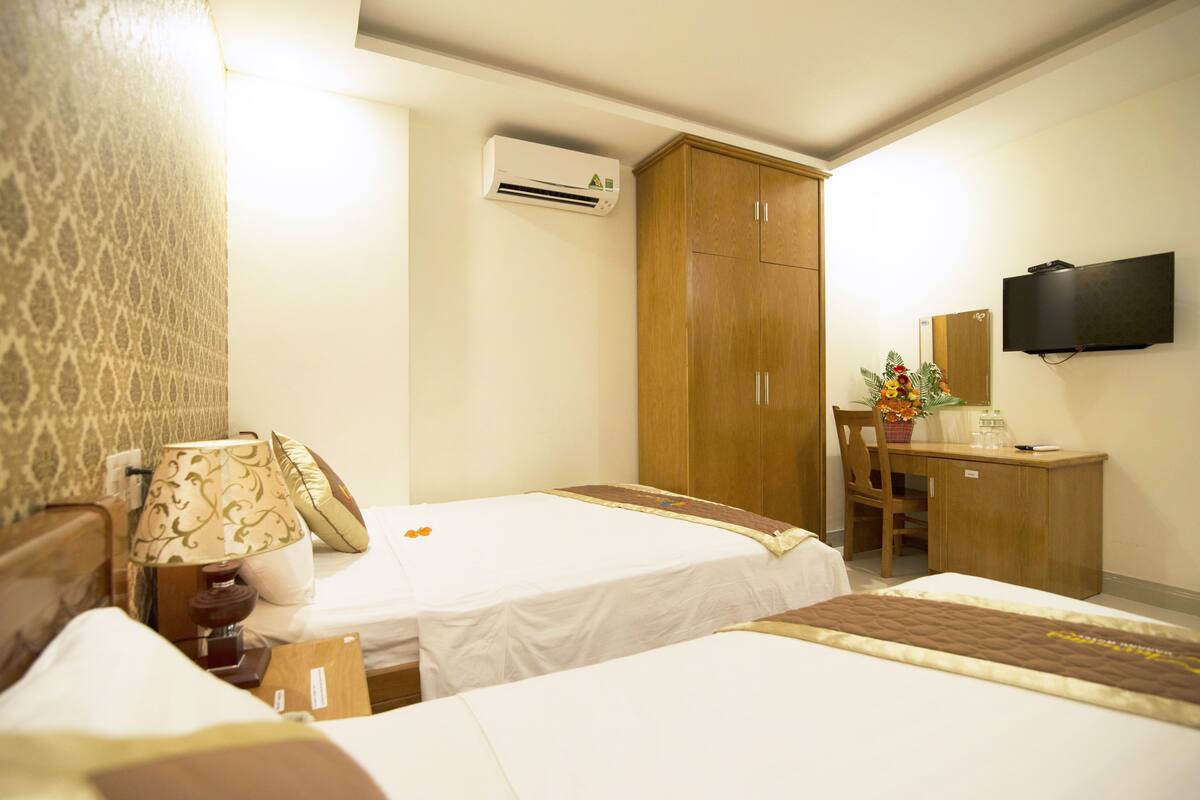 A hotel room with two beds, a desk, a chair, a TV, an air conditioning unit, and a patterned wall.
