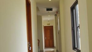 Un pasillo con una puerta de madera a la izquierda, una ventana a la derecha y otra puerta al final.