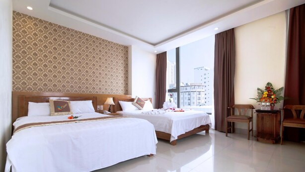 Habitación de hotel con dos camas, un ventanal grande, un escritorio con silla y una planta decorativa.