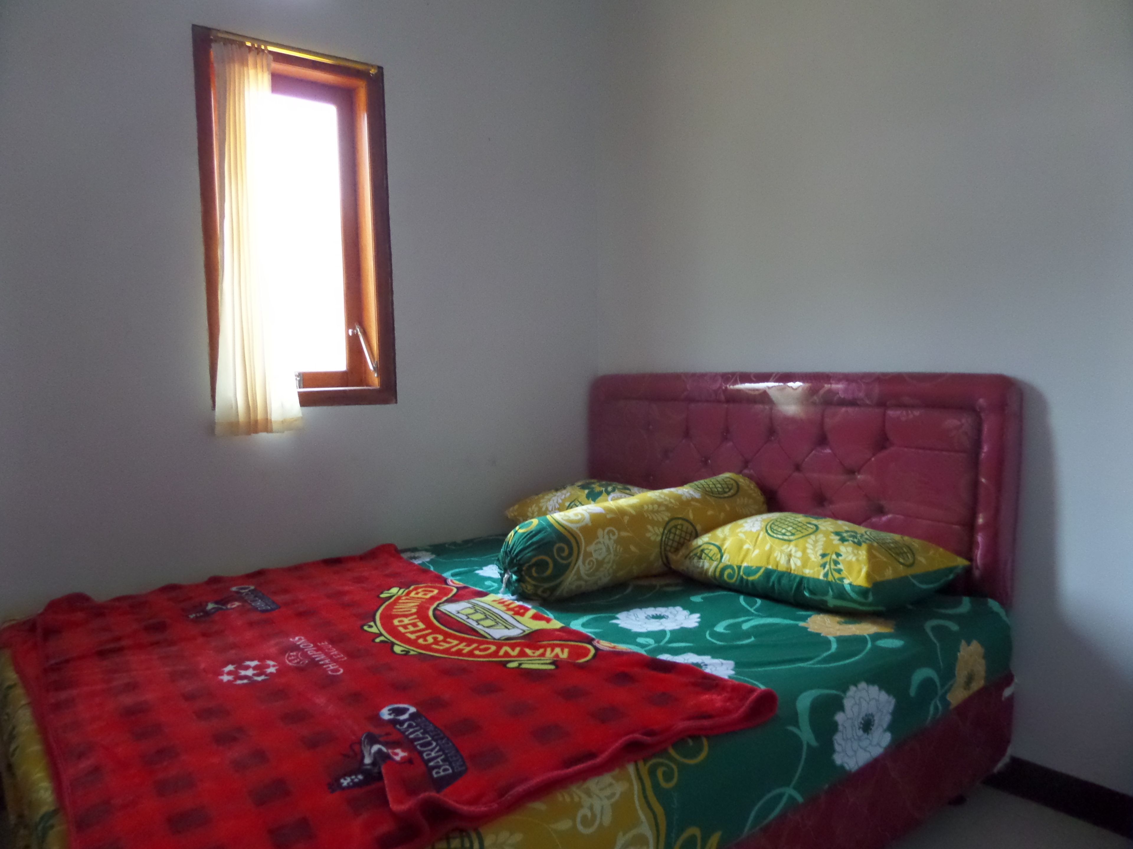 Ein Einzelbett mit rotem Kopfteil und einer blumigen Bettdecke, eine rote Decke mit Sportteam-Logos und ein Fenster mit Vorhängen.