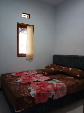 A bedroom with a bed, a window with a curtain, and a wall-mounted light fixture. - Agung Safira Homestay (Ngadisari)