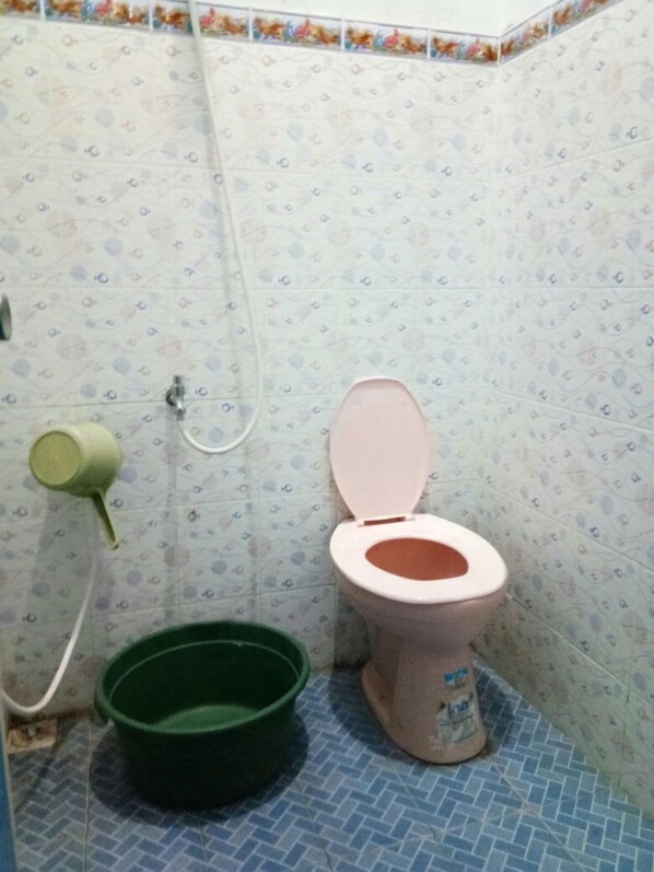 Un baño pequeño con inodoro, un cubo verde y una manguera de ducha.
