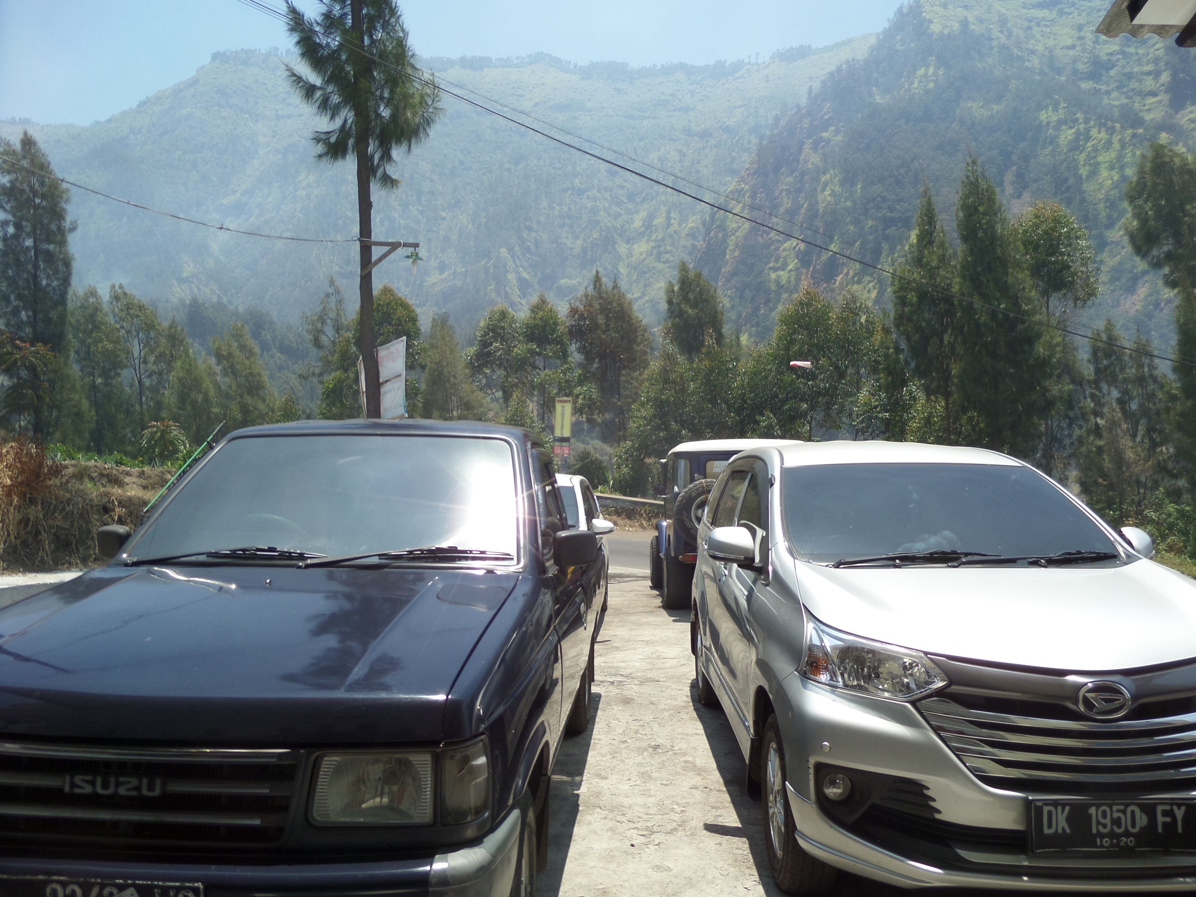 Two parked cars, a black Isuzu and a silver Isuzu, on a road with a mountainous backdrop.