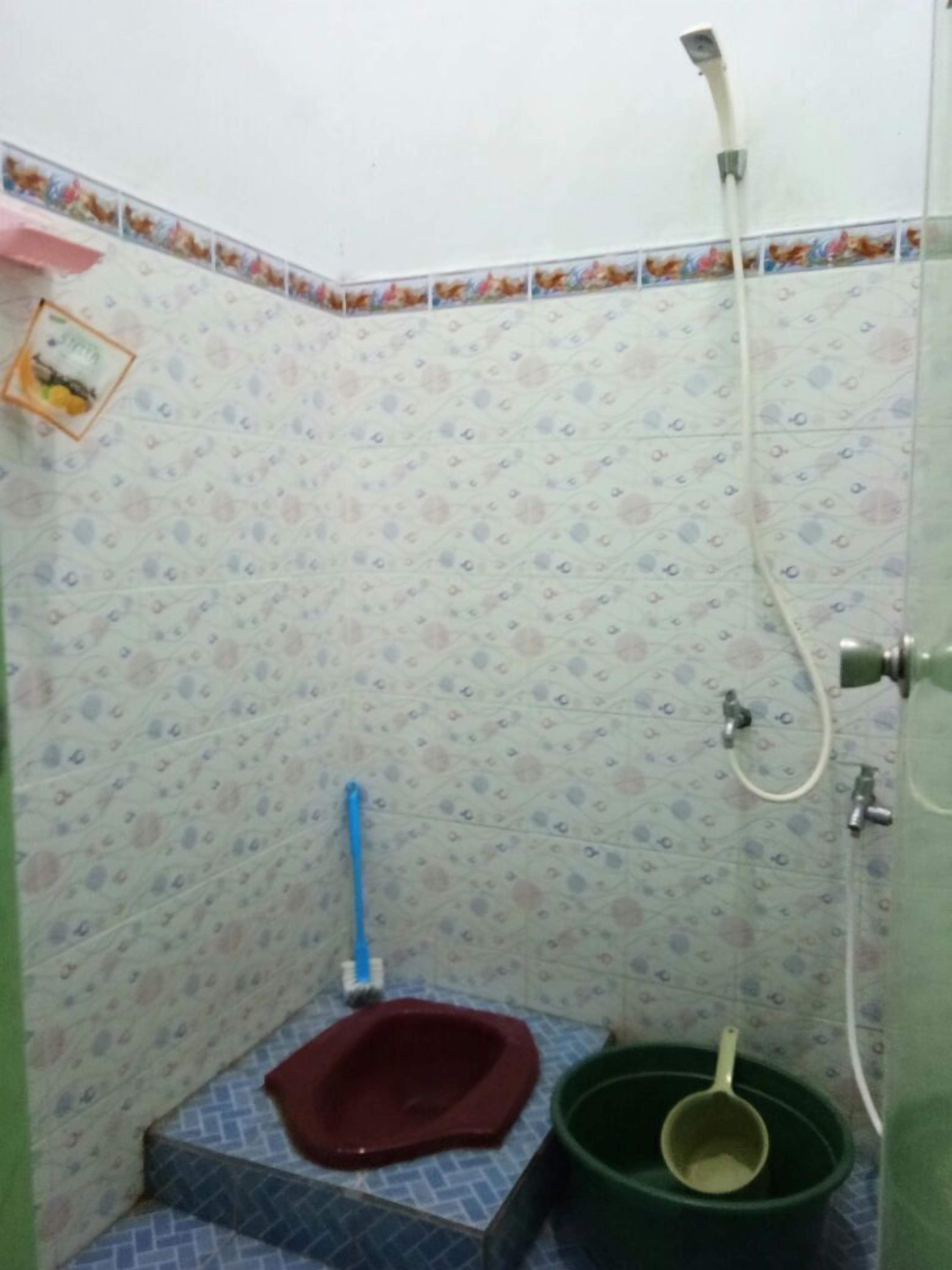 A small bathroom with a toilet, a shower, and a green bucket.