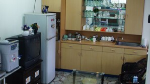 A compact kitchen with a refrigerator, microwave, and a small dining table with chairs. - The Lodge for Cyclists - Hostel (Fangliao)
