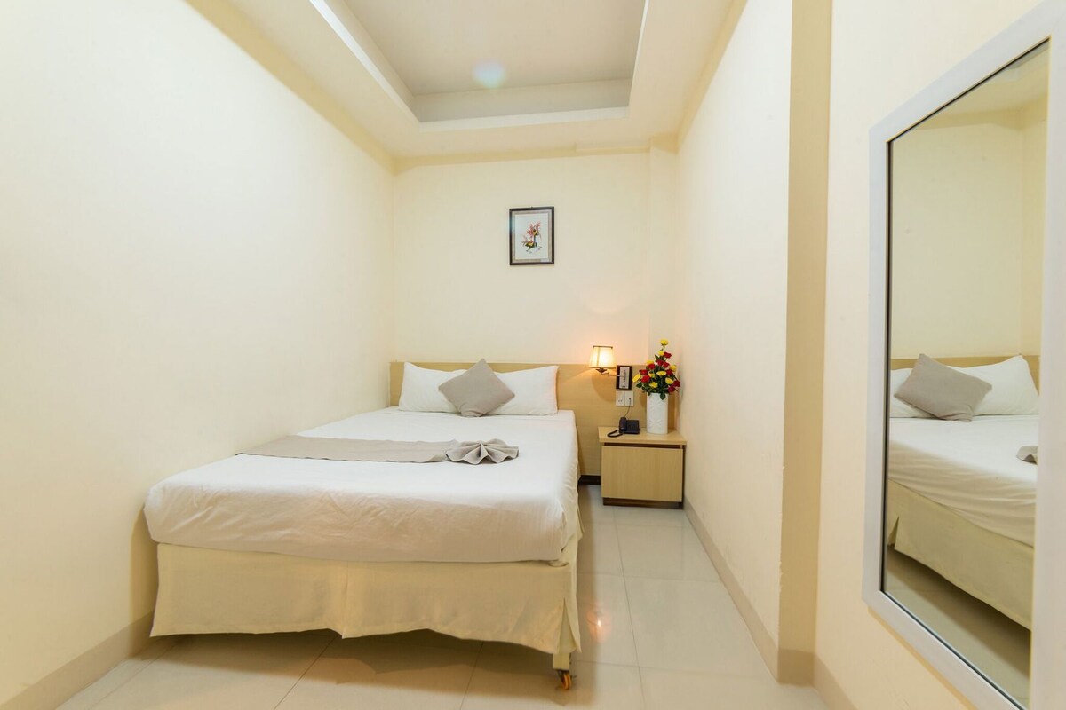 A bedroom with a bed, bedside table, lamp, and a mirror.