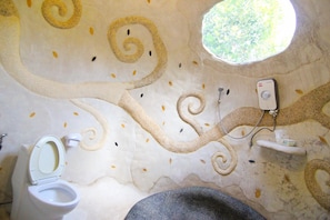 A bathroom with a unique ceiling design featuring swirling patterns and a small window. - Naidee Sculptured Huts (Hua Hin)