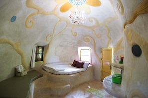 A uniquely designed room with a bed, a small window, and a door. - Naidee Sculptured Huts (Hua Hin)