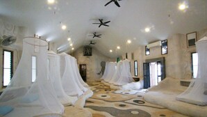 A room with four beds covered in white canopies, a patterned carpet, and ceiling fans. - Naidee Sculptured Huts (Hua Hin)