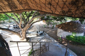 A tree-lined outdoor area with a thatched roof, a staircase, and a seating area with tables and chairs. - Naidee Sculptured Huts (Hua Hin)