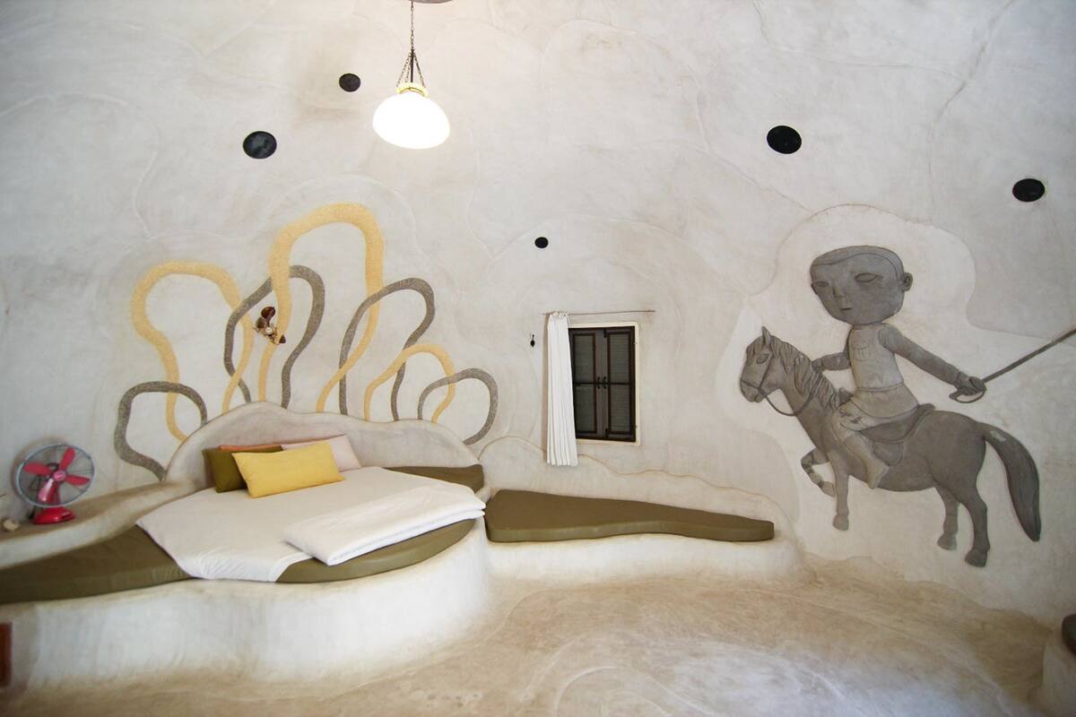 A room with a bed, a small window, and a mural of a person on a horse.