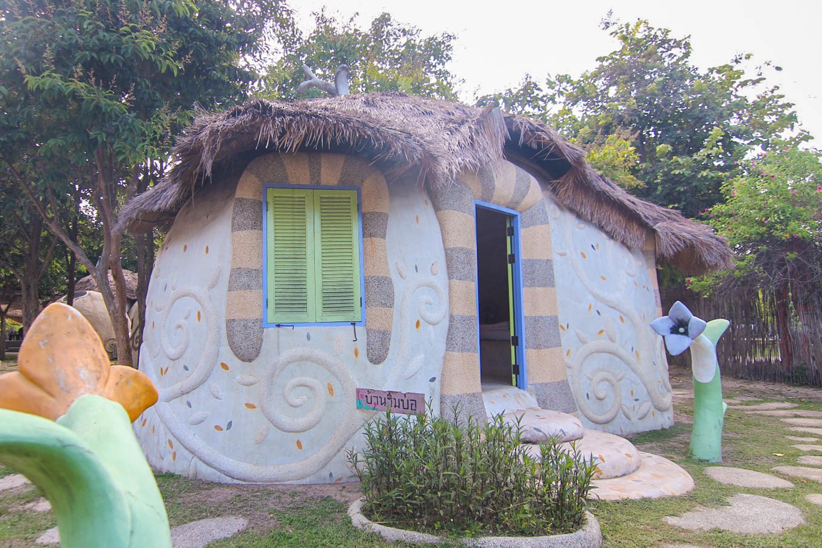 A house with a thatched roof, green shutters, and a decorative sign in a foreign language.