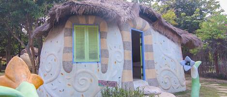 A house with a thatched roof, green shutters, and a decorative sign in a foreign language.