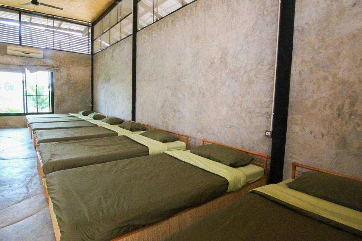 A dormitory room with four single beds aligned against a wall, each with a pillow and a blanket.