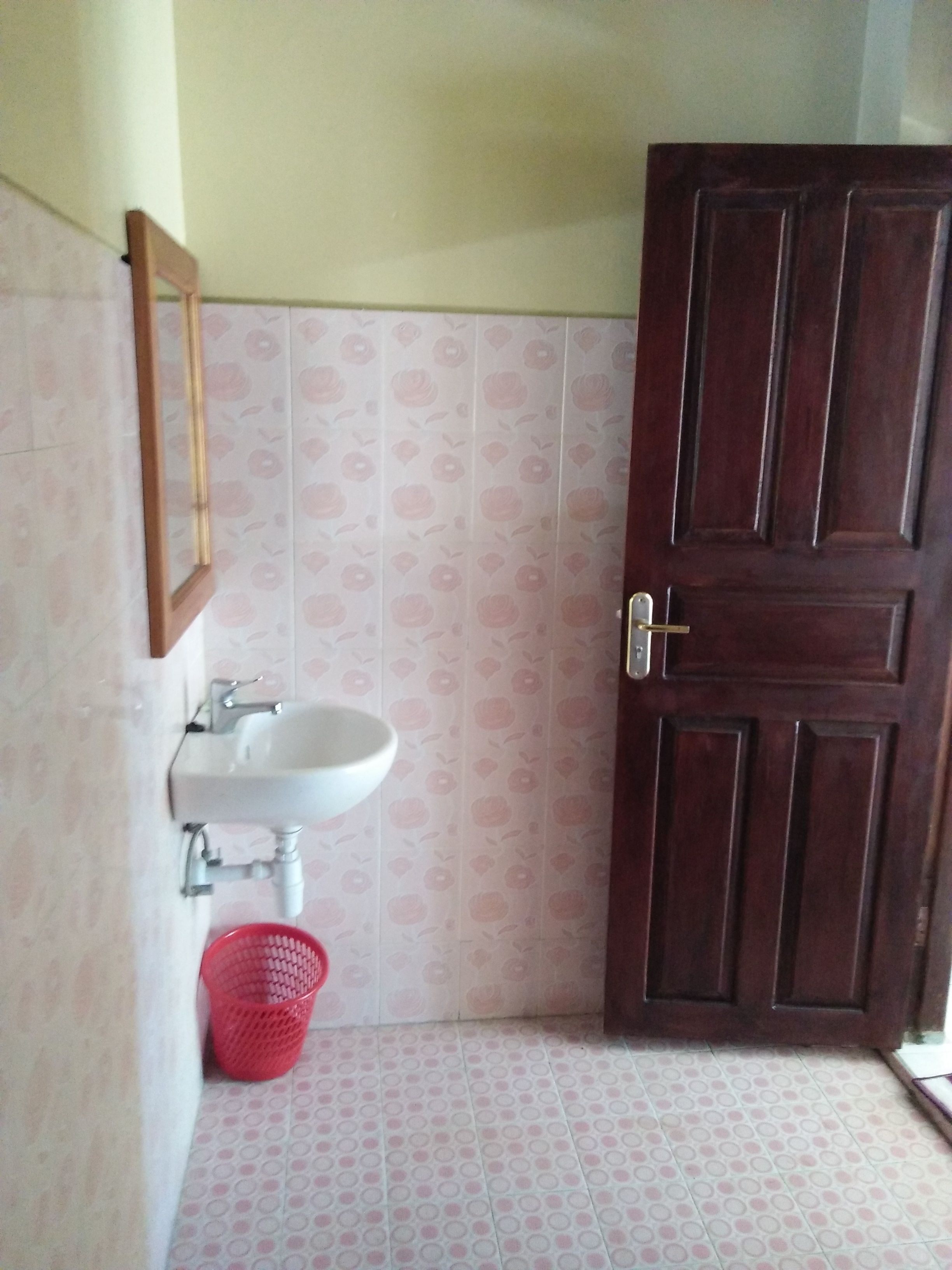 A bathroom with a white sink, a mirror, a red basket, and a wooden door.