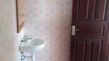A bathroom with a white sink, a mirror, a red basket, and a wooden door.