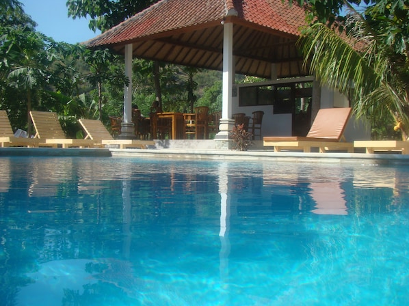 Una piscina con sillones de descanso y una zona de estar cubierta.