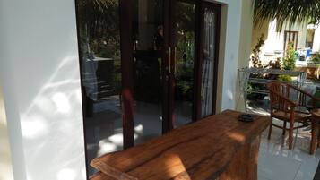 Una mesa y sillas de madera en una habitación iluminada por el sol, con un ventanal corredizo que da a un espacio exterior con plantas y vistas al cielo.