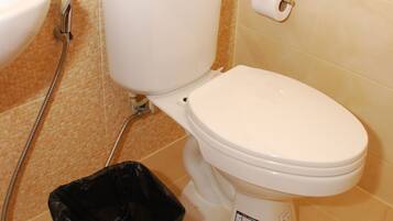 Un baño con inodoro, bidé, cubo de basura y dispensador de papel higiénico.