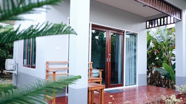 A modern house with a wooden bench outside, a sliding glass door, and lush greenery. - Pran Kiang Lay (Pranburi)