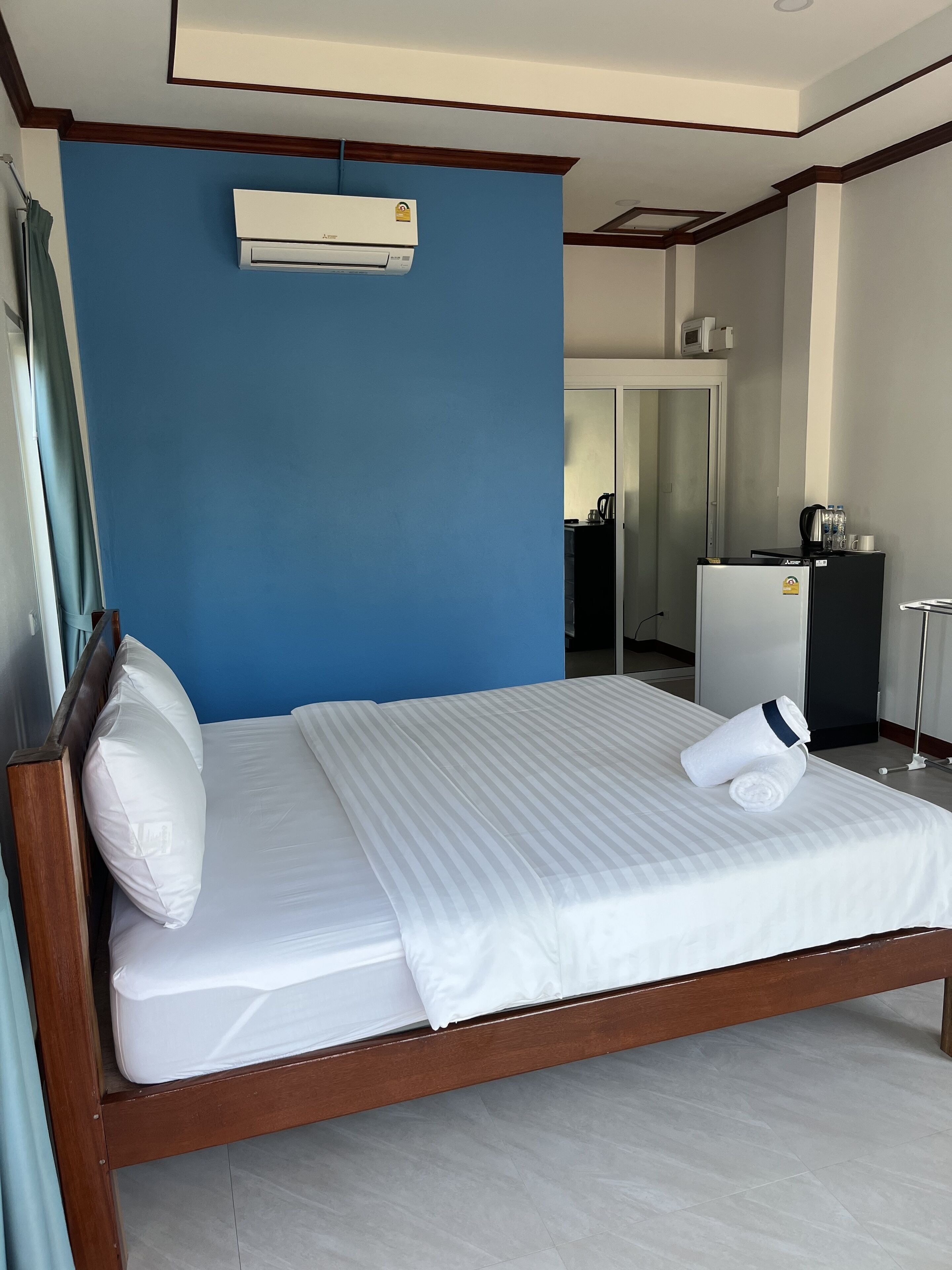 Habitación de hotel con cama, pared azul, aire acondicionado, armario y una pequeña kitchenette.
