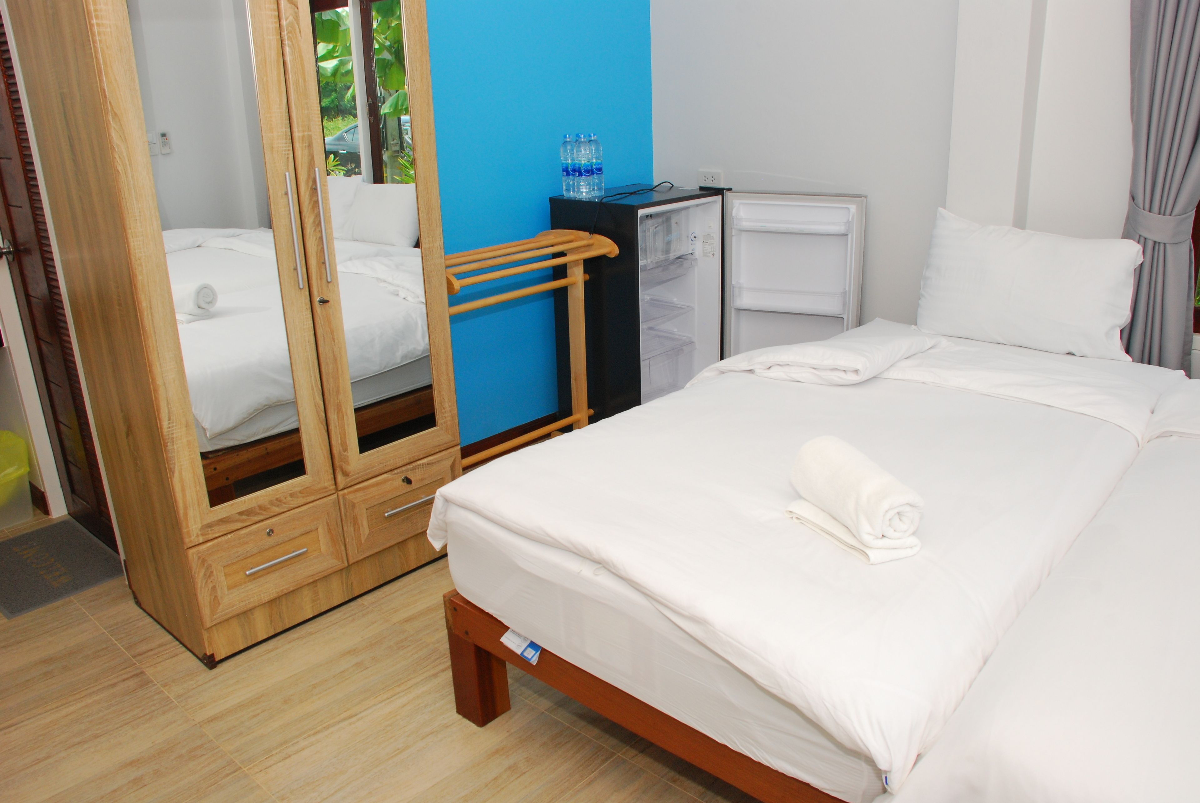 Habitación de hotel con cama, armario, mini refrigerador y dispensador de agua.