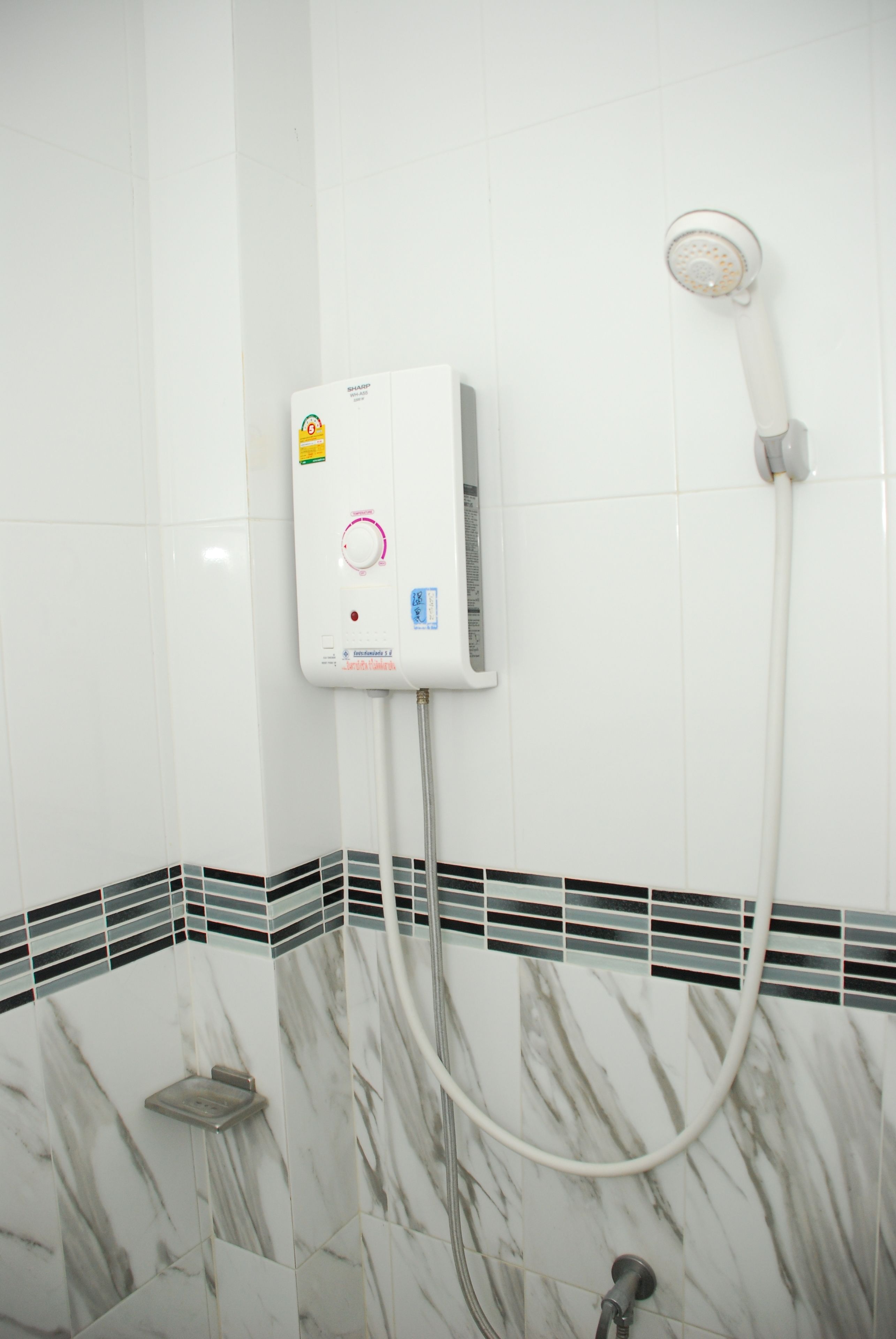 A bathroom with a white tiled wall, a shower unit with a control panel, and a tiled floor with a marble pattern.