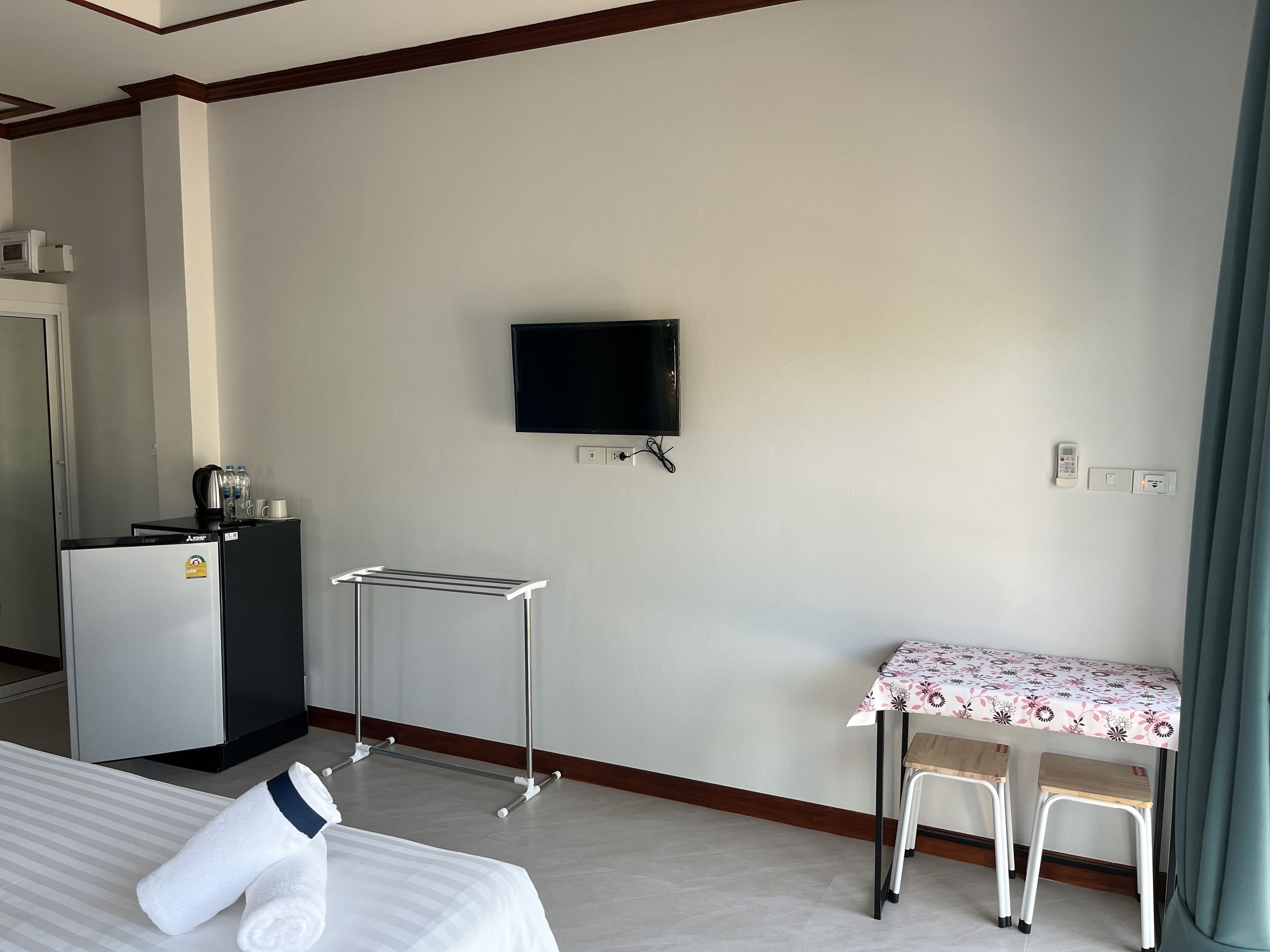 Une chambre d’hôtel comprenant un lit, un bureau avec une table, un téléviseur fixé au mur, un minibar et une fenêtre avec des rideaux.
