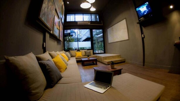 A modern lounge area with a sofa, a laptop, and a TV. - In A Box Hostel (Bangkok)