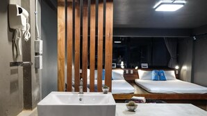 A modern hotel room with a large rectangular sink, wooden slats, two beds with white bedding, and a small bedside table with a plant. - In A Box Hostel (Bangkok)