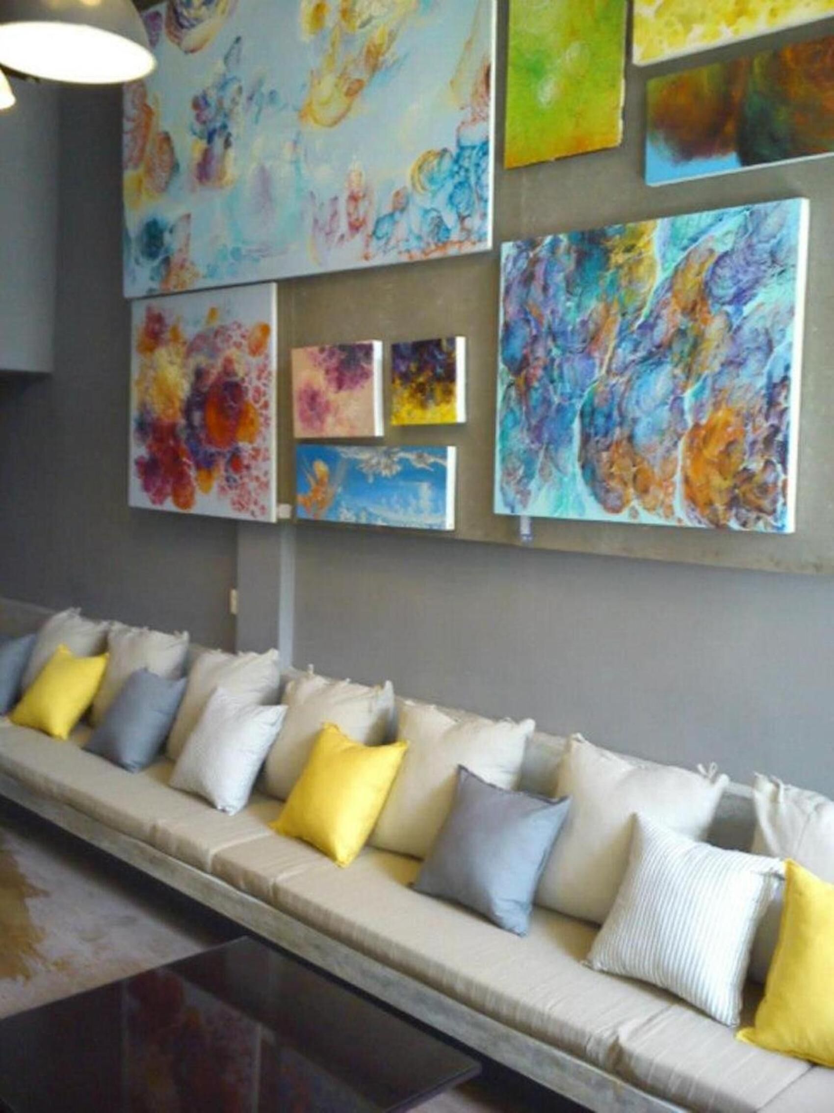 A modern interior with a long sofa adorned with colorful cushions, a wall decorated with abstract paintings, and a polished floor.