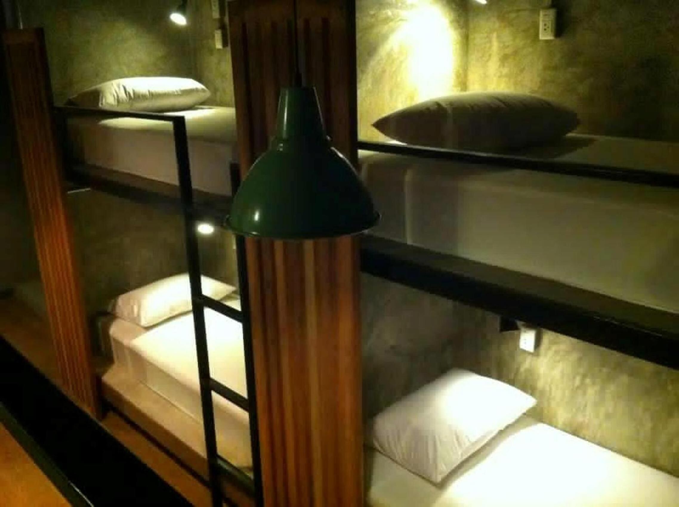 A bunk bed with a green lamp, wooden paneling, and a white pillow.