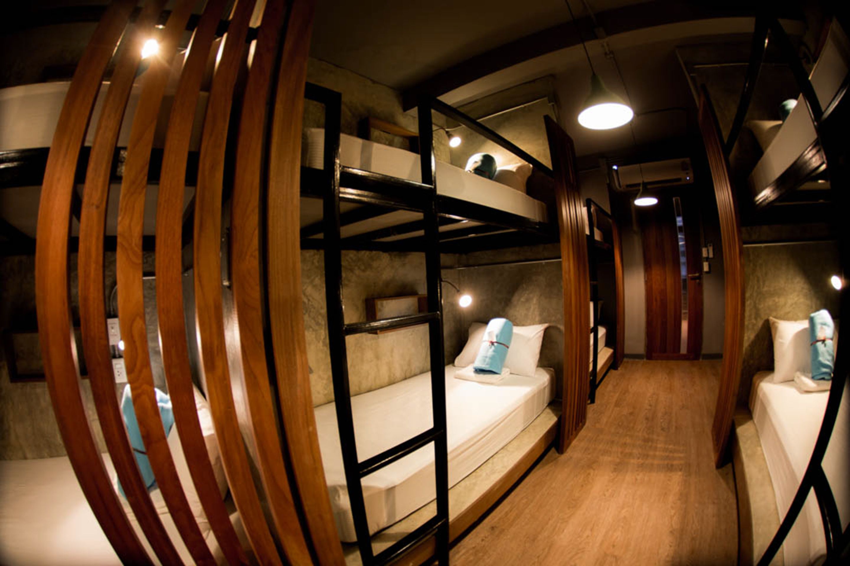 A bunk bed room with wooden slats, a wooden floor, and a ceiling light.