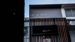 A building with a sign that reads "in-a-box" and a window with vertical wooden slats. - In A Box Hostel (Bangkok)