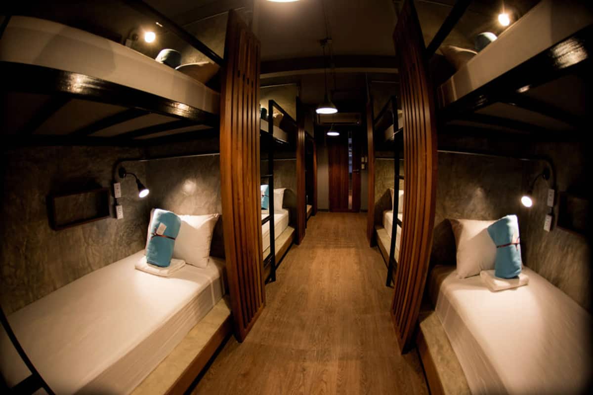 A narrow corridor with bunk beds on either side, wooden paneling, and overhead lighting.
