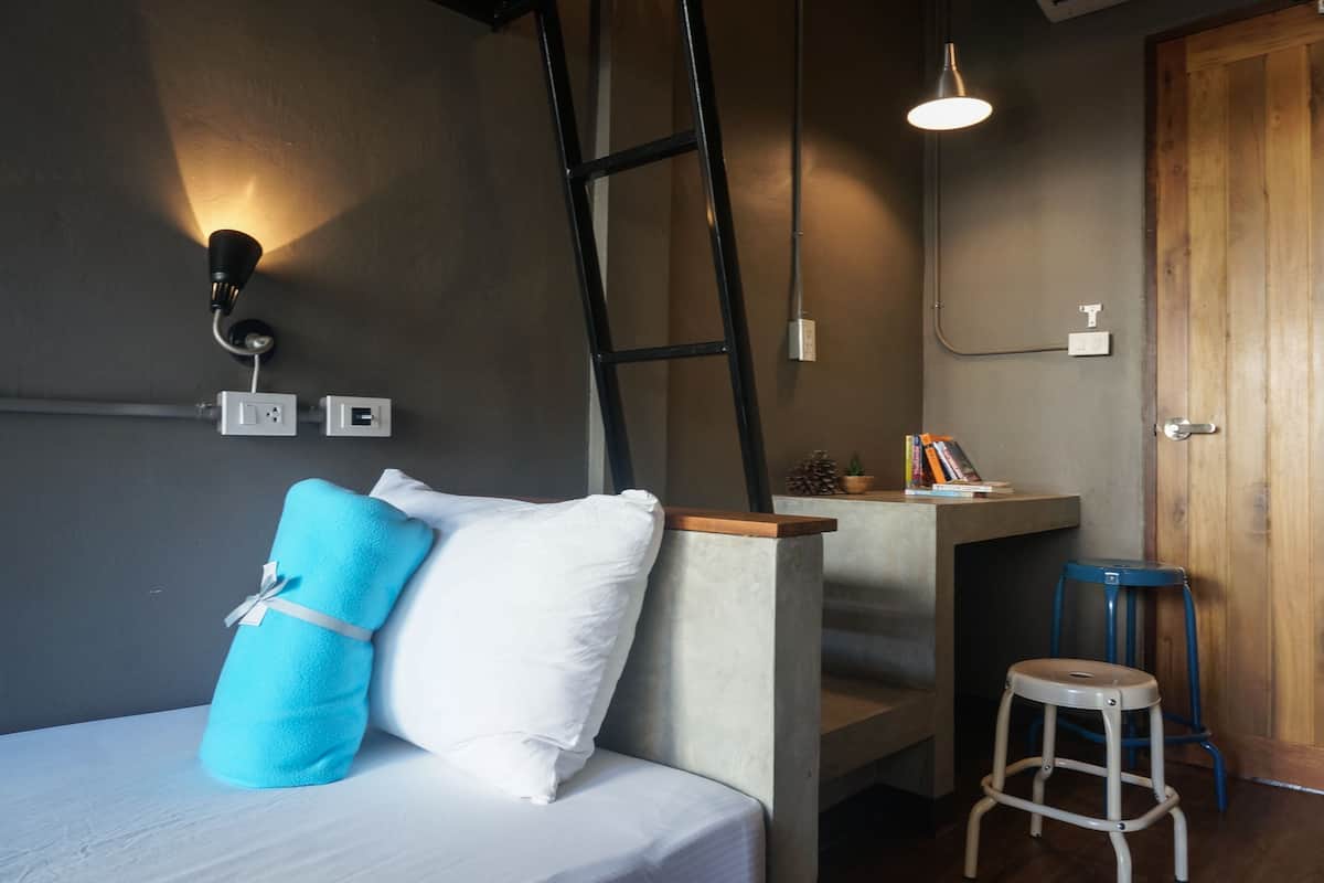 A bedroom with a bed, a desk, a ladder, and a stool.