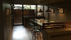 A modern kitchen with a long island, bar stools, pendant lighting, and a view through the windows. - In A Box Hostel (Bangkok)